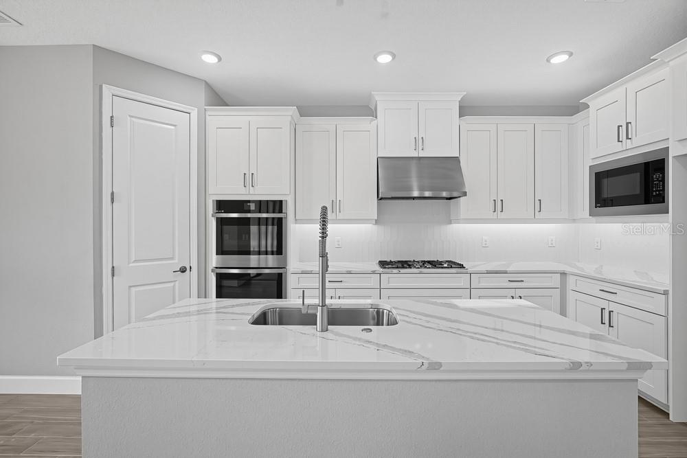 A bright kitchen features a large white island with four gray stools and stainless appliances — 16237 ALPHA GROVE PLACE, ODESSA, FL