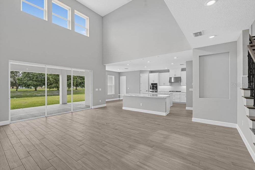 A bright, open-concept living room and kitchen featuring high ceilings, light wood floors, and a pool — 16237 ALPHA GROVE PLACE, ODESSA, FL