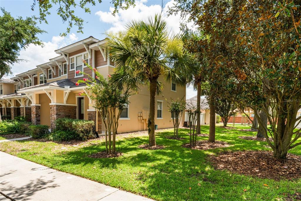 A two-story townhouse exterior features tan stucco, brown siding, stone accents, and a covered porch — 7327 MILLSTONE STREET, WINDERMERE, FL