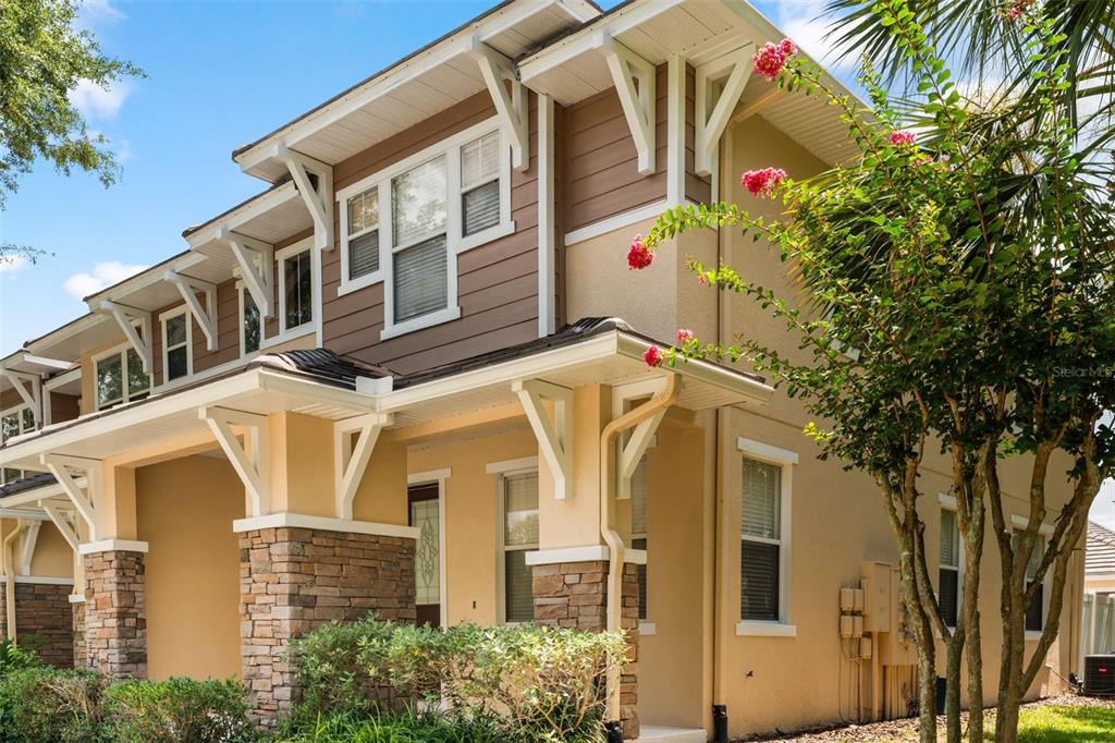 A covered front porch features a brown front door, stone pillar, and beige stucco walls — 7327 MILLSTONE STREET, WINDERMERE, FL