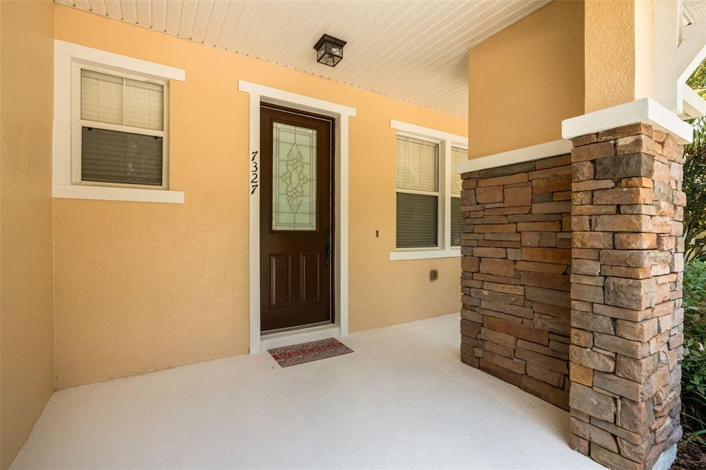 A covered front porch features stone-clad columns and a view of a grassy park area — 7327 MILLSTONE STREET, WINDERMERE, FL