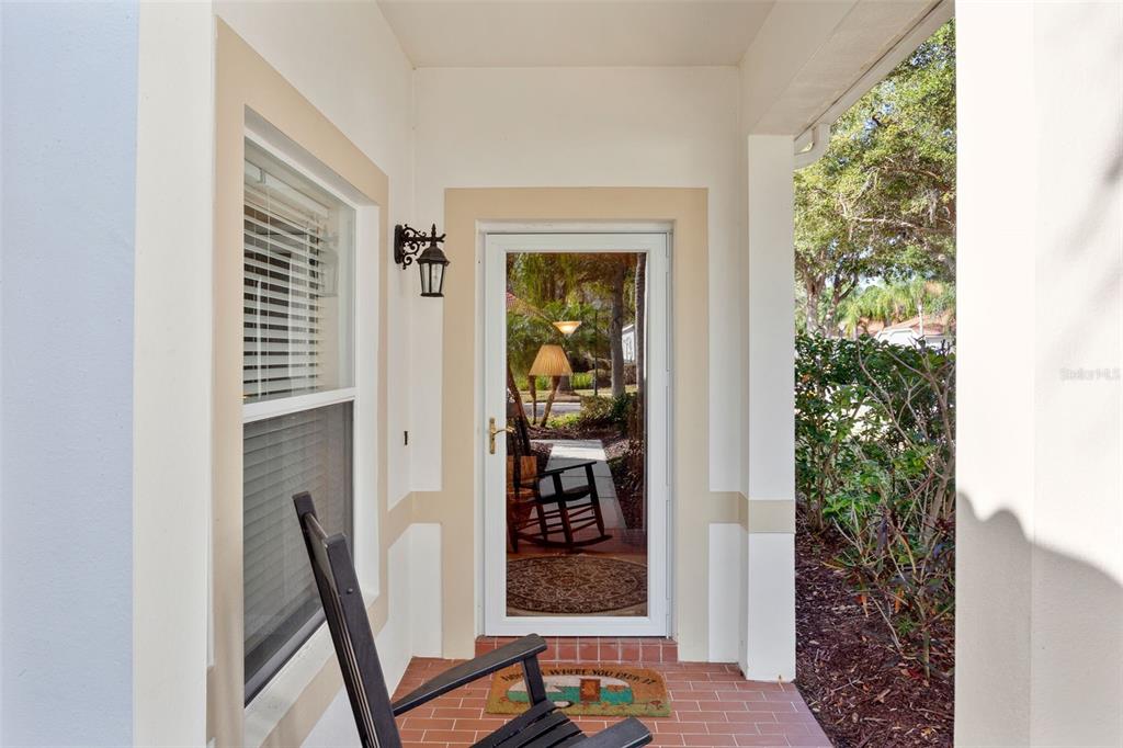 A covered front porch features a brick floor, a rocking chair, and a glass storm door — 10245 DEVONSHIRE LAKE DRIVE, TAMPA, FL