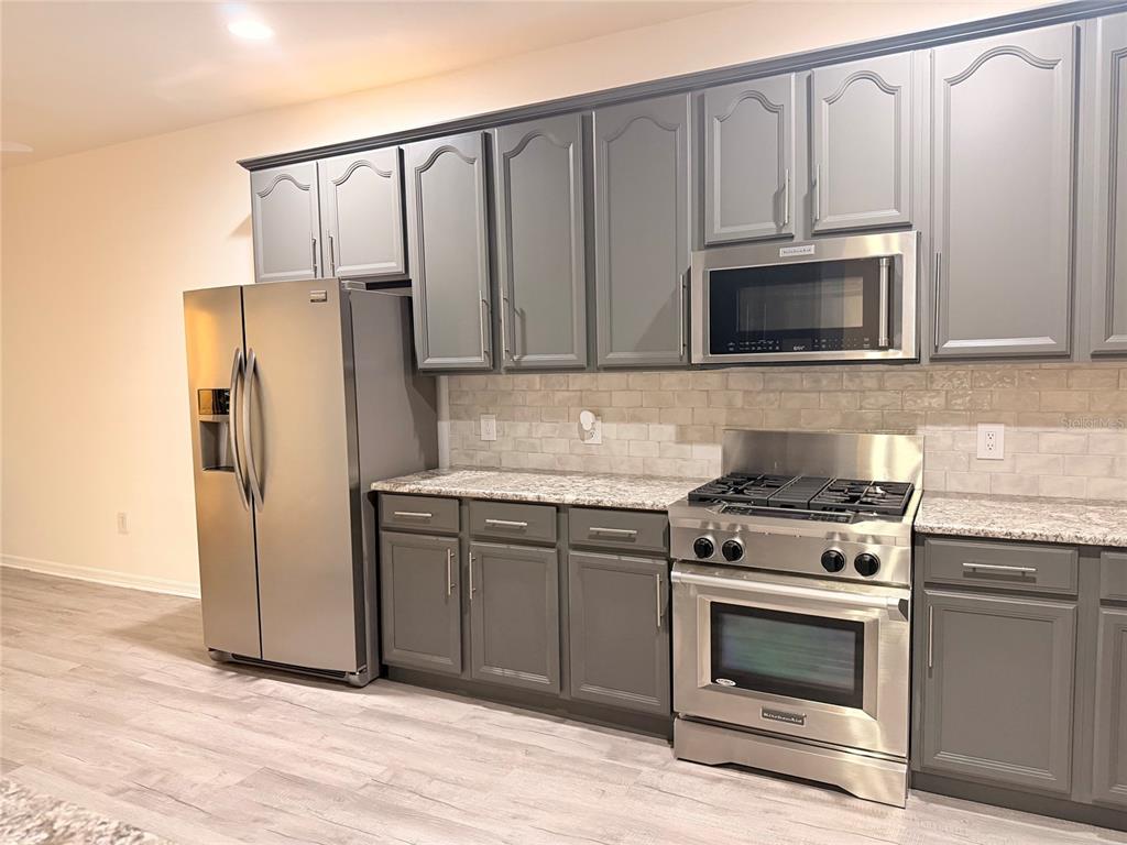 A kitchen featuring gray cabinets, stainless steel appliances, granite countertops, and a subway tile backsplash — 10245 DEVONSHIRE LAKE DRIVE, TAMPA, FL