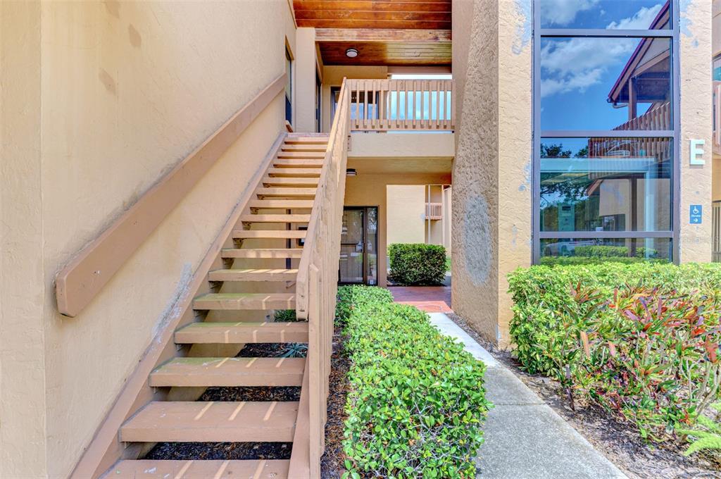 An exterior view of a multi-story apartment building featuring wooden stairs and landscaped bushes — 2831 RINGLING BOULEVARD UNIT E214, SARASOTA, FL