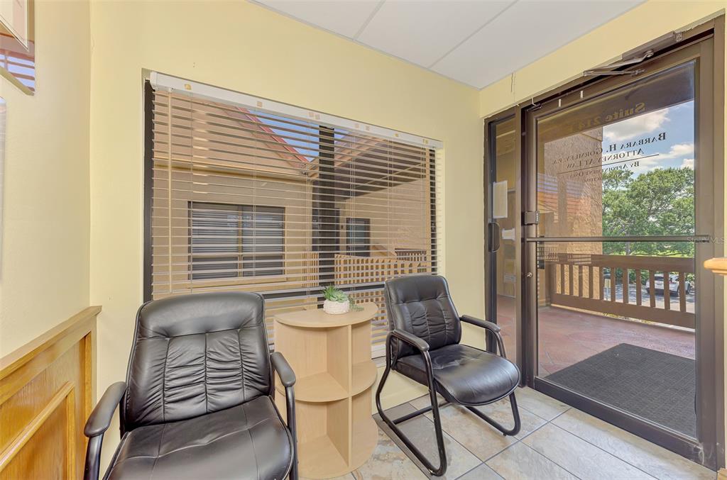 A waiting area features two black leather chairs, a small corner table, and a glass door — 2831 RINGLING BOULEVARD UNIT E214, SARASOTA, FL