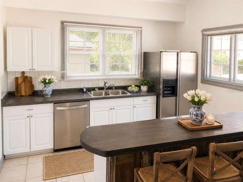 A kitchen features white cabinets, dark countertops, stainless steel appliances, and a wooden island with chairs — 2107 W CHESTNUT STREET, TAMPA, FL