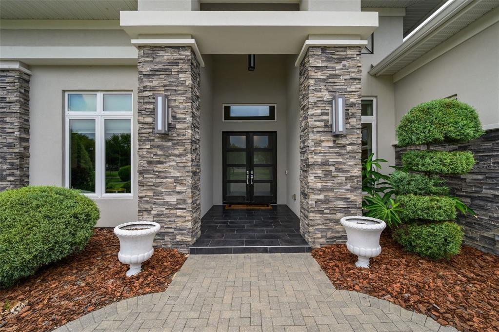 A stone-clad entryway features a double glass door, tiled porch, and two white decorative planters — 2807 SW 117TH STREET, GAINESVILLE, FL