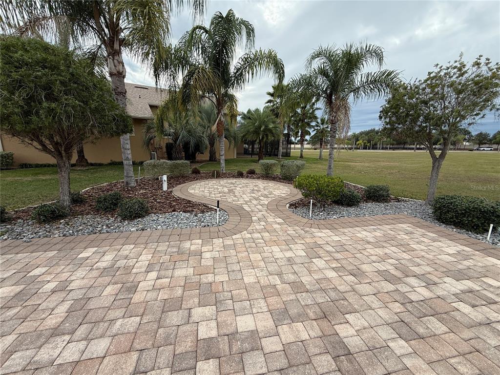 A paved patio area features a circular design surrounded by landscaping and palm trees — 346 NOLANE LANE, POLK CITY, FL