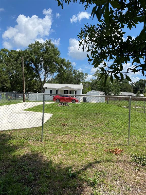 A red car is parked in front of a small house behind a chain-link fence — 1835 W GREENWOOD STREET, LAKELAND, FL