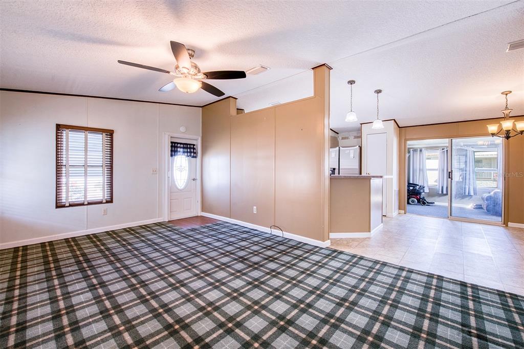 A living room with plaid carpeting, a ceiling fan, and an adjacent tiled kitchen area — 403 BLUE MARLIN DRIVE, OLDSMAR, FL