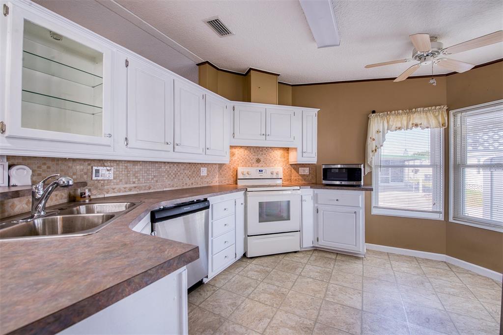 A kitchen features white cabinets, a double sink, white appliances, and tan tile flooring — 403 BLUE MARLIN DRIVE, OLDSMAR, FL