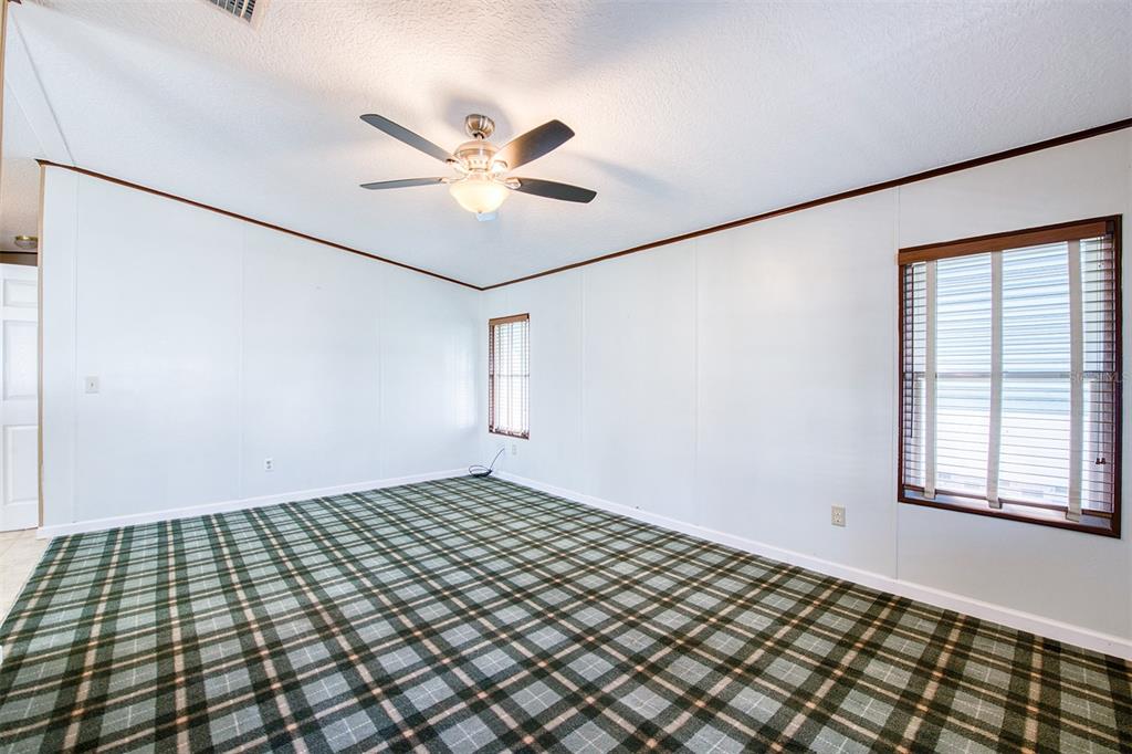 An empty room features white walls, a ceiling fan, and green plaid carpeting — 403 BLUE MARLIN DRIVE, OLDSMAR, FL