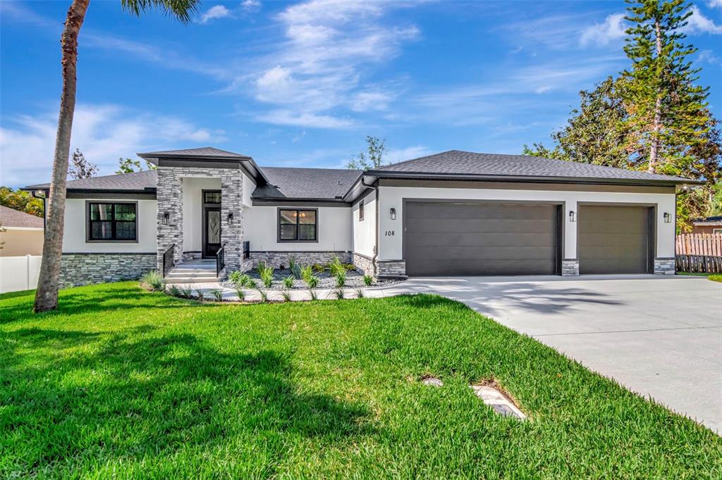 A modern single-story house with white stucco walls, stone accents, and a two-car garage — 108 IRWIN STREET E, SAFETY HARBOR, FL