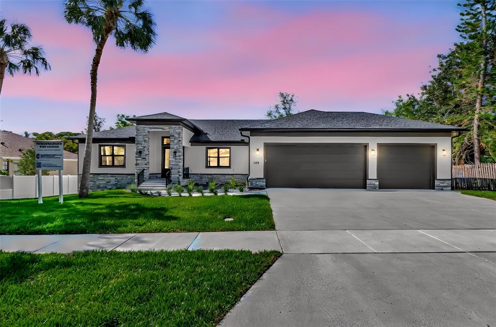 A modern single-story house features white stucco walls, stone veneer accents, and a dark roof — 108 IRWIN STREET E, SAFETY HARBOR, FL