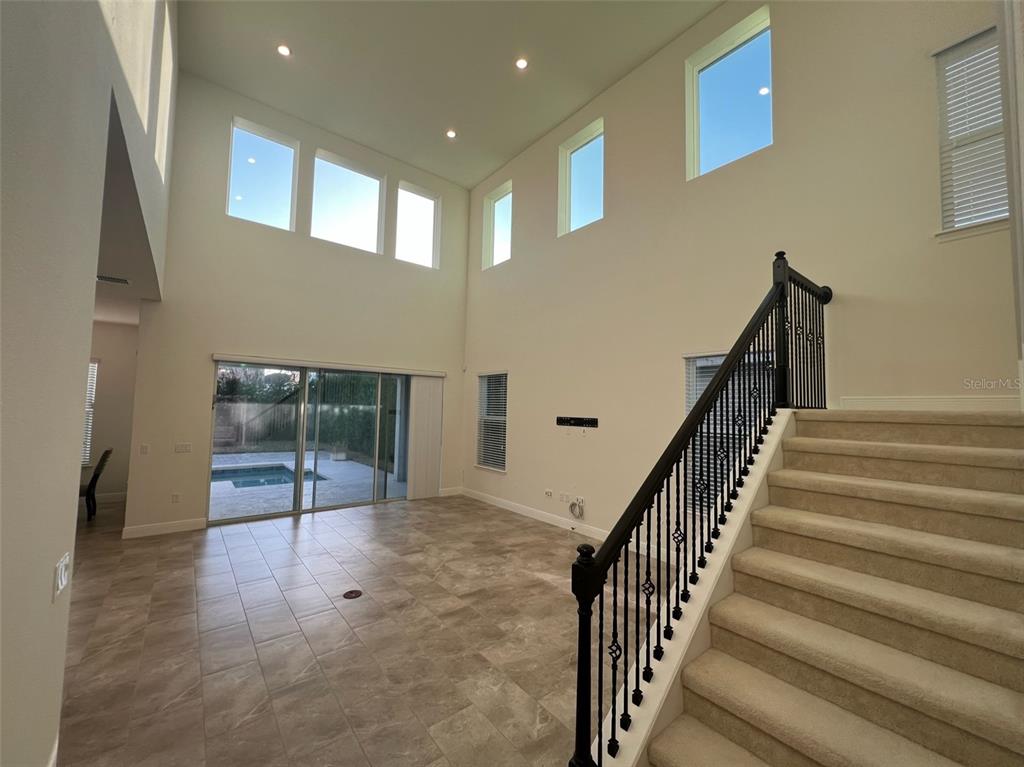 A living room with high ceilings, tile flooring, a staircase, and sliding glass doors to a pool — 8794 CRESCENDO AVENUE, WINDERMERE, FL
