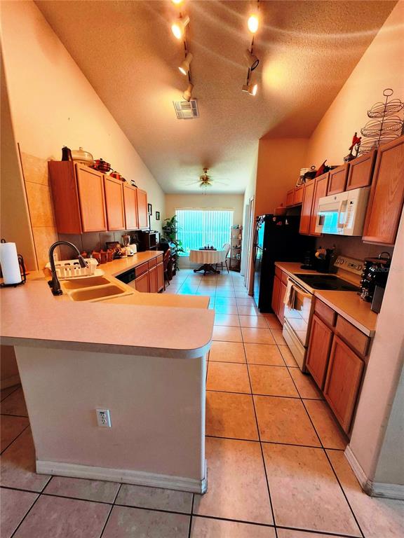 A kitchen with wood cabinets, tile floors, and a breakfast bar overlooking a dining area — 4613 EAGLET LANE, KISSIMMEE, FL