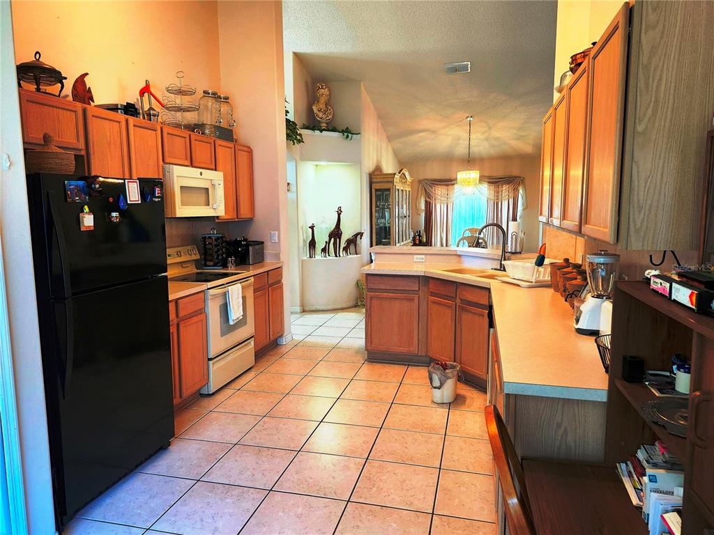 A kitchen with wood cabinets, tile flooring, a black refrigerator, and a breakfast bar — 4613 EAGLET LANE, KISSIMMEE, FL