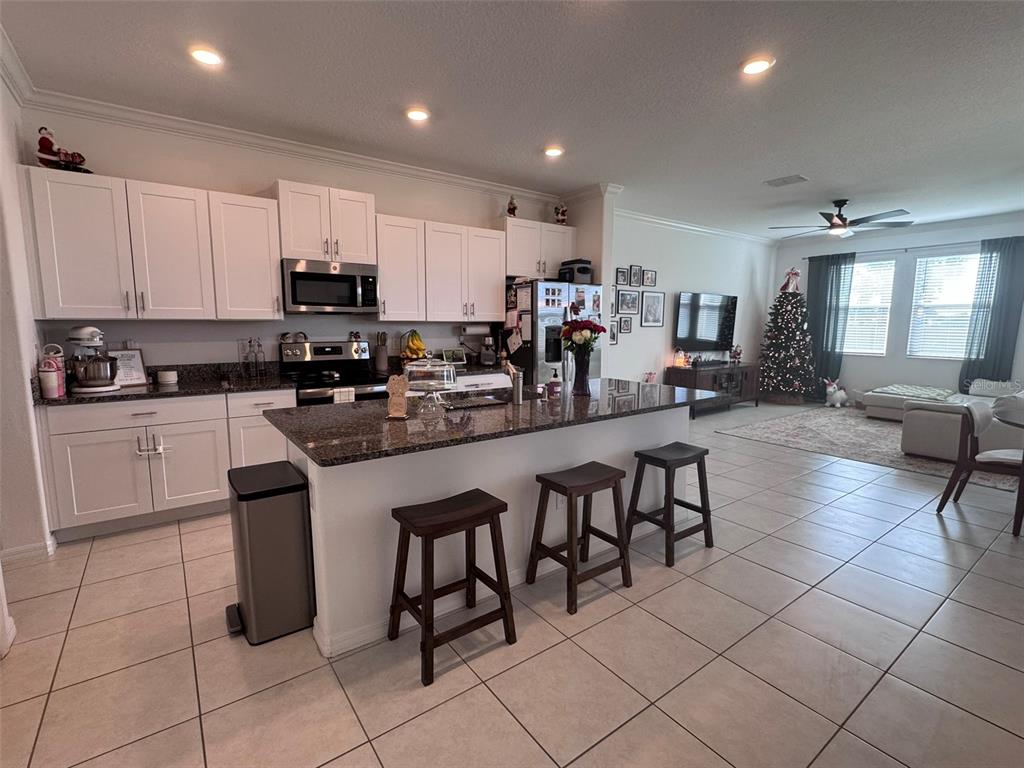 A kitchen with white cabinets, granite countertops, and an island with three bar stools — 31779 BLUE PASSING LOOP, WESLEY CHAPEL, FL