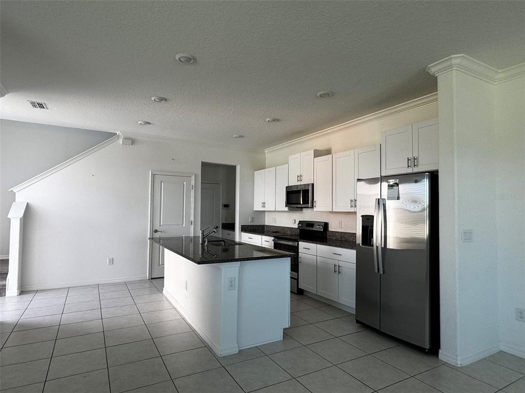 A kitchen features white cabinets, stainless steel appliances, a dark granite island, and tiled floors — 31779 BLUE PASSING LOOP, WESLEY CHAPEL, FL