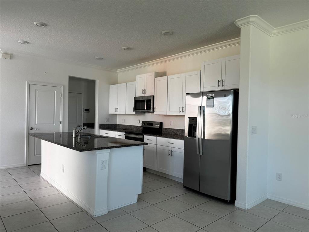 A kitchen features white cabinets, granite countertops, a center island, and stainless steel appliances — 31779 BLUE PASSING LOOP, WESLEY CHAPEL, FL