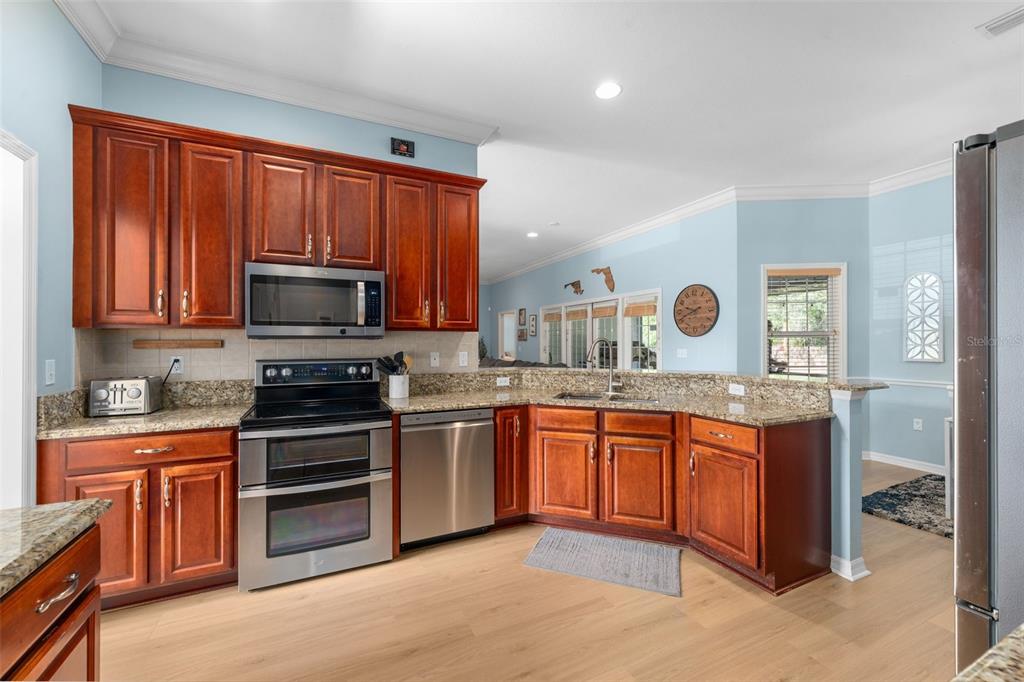 A kitchen features cherry wood cabinets, granite countertops, stainless steel appliances, and light blue walls — 6940 SW 86TH TERRACE, GAINESVILLE, FL