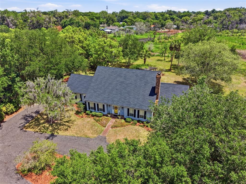 A gray house with black shutters sits behind a large tree and gravel driveway — 1245 WESTOAK DRIVE, DELAND, FL