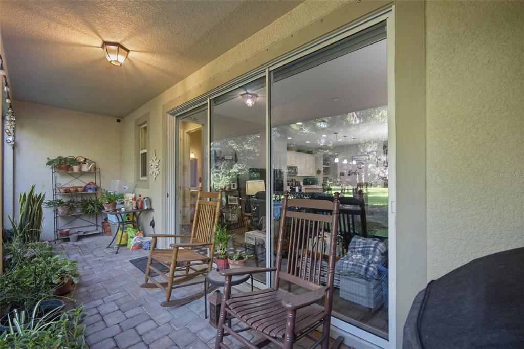 A covered patio features brick pavers, two rocking chairs, and a sliding glass door — 14215 PONDHAWK LANE, TAMPA, FL