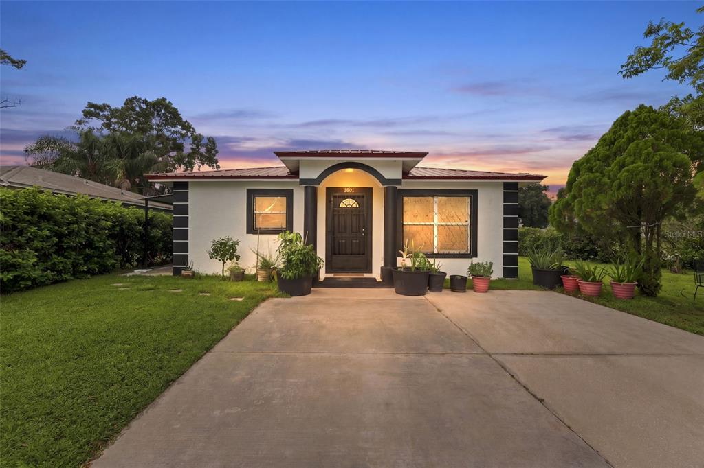 A single-story house with a white exterior, dark trim, and a concrete driveway at sunset — 1801 BETHUNE DRIVE, PLANT CITY, FL