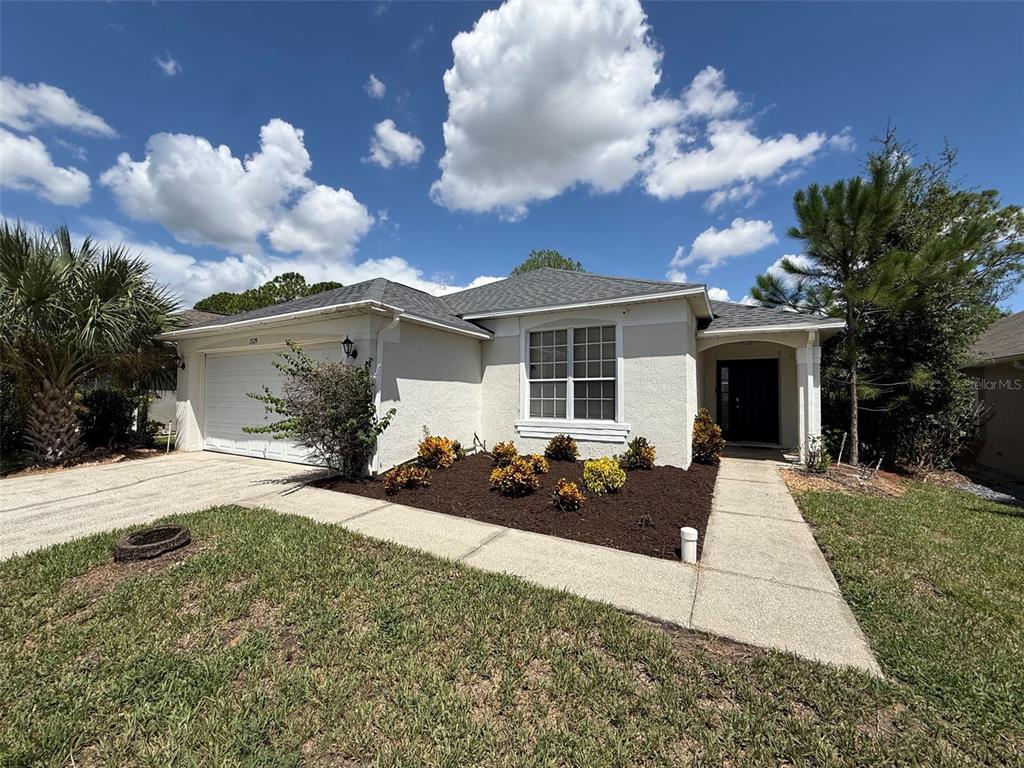The exterior of a single-story house features a light-colored stucco facade, a gray roof, and landscaping — 1529 GULF VUE DRIVE, HAINES CITY, FL