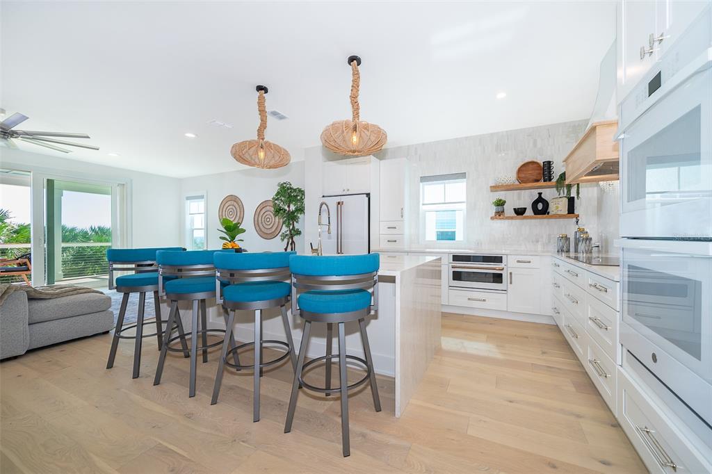 A modern kitchen features white cabinetry, a waterfall island with blue stools, and light wood flooring — 204 SURFVIEW LANE, PALM COAST, FL