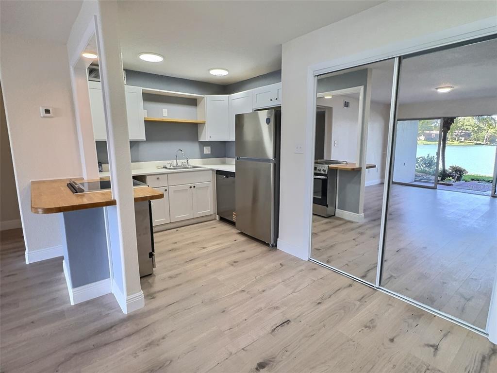 A kitchen with white cabinets, stainless steel appliances, and wood-look flooring opens to a living area — 620 ORANGE DRIVE UNIT 225, ALTAMONTE SPRINGS, FL