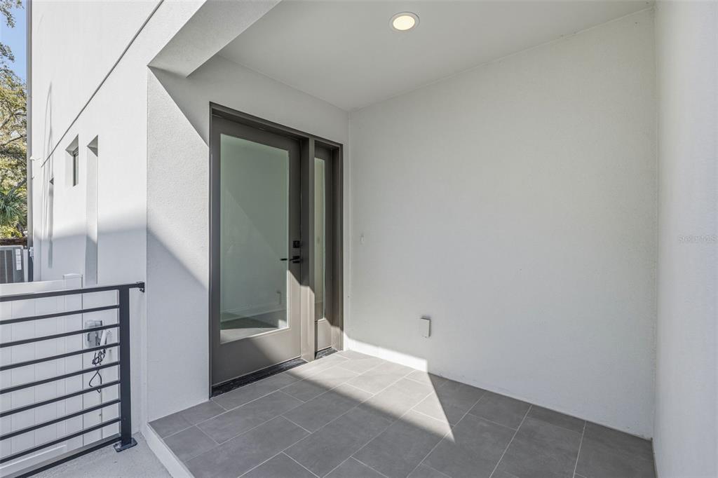 A modern covered entryway features gray tiled flooring, white walls, and a glass-paneled door — 4509 W NORTH A STREET UNIT 2, TAMPA, FL