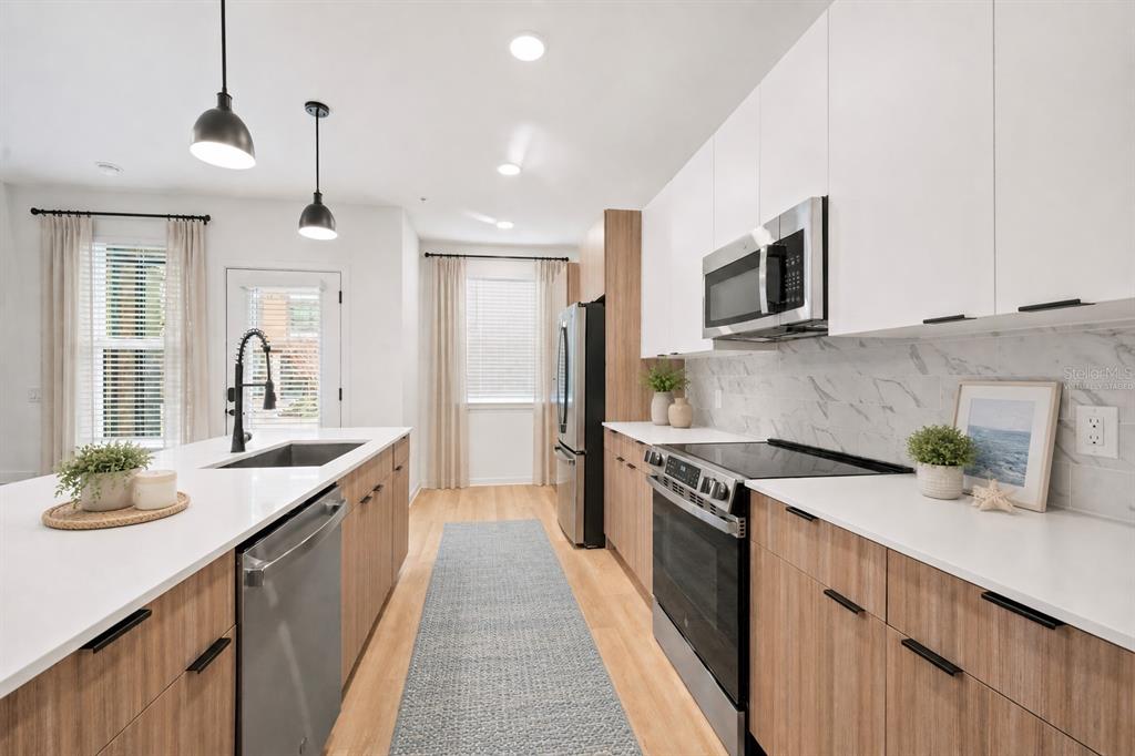 A modern kitchen features wood-tone cabinets, white countertops, stainless steel appliances, and a central island — 2285 CROWN VILLAGE ROAD UNIT TH1, OCOEE, FL
