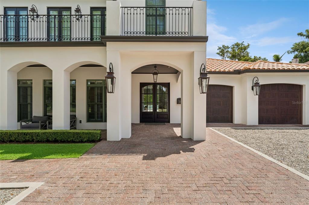 A paved driveway leads to the arched entryway and two garage doors of a stucco home — 276 DETMAR DRIVE, WINTER PARK, FL
