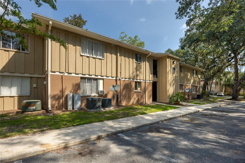 A two-story apartment building with tan vertical siding and brick lower walls sits near parking — 507 NW 39TH ROAD UNIT 122, GAINESVILLE, FL