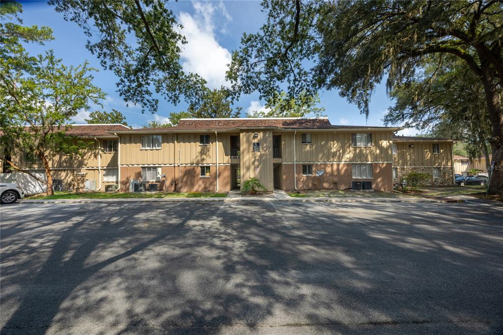 A two-story apartment building with tan siding and a parking lot in the foreground — 507 NW 39TH ROAD UNIT 122, GAINESVILLE, FL
