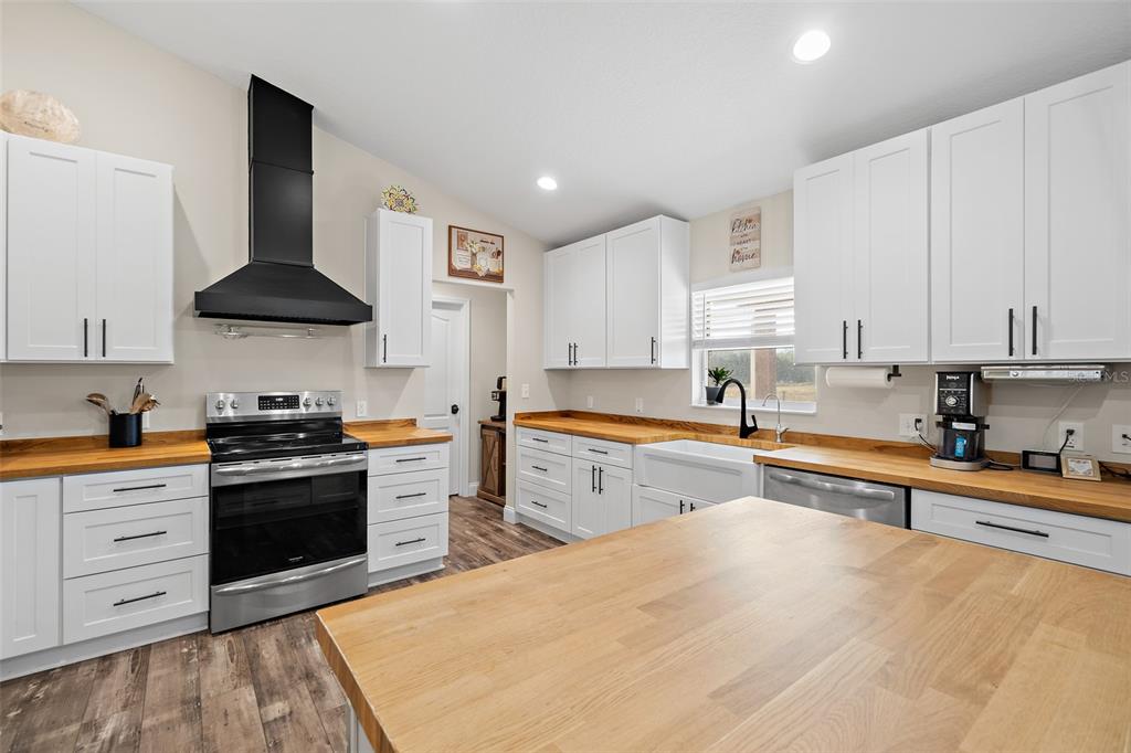 A kitchen features white cabinets, butcher block countertops, a black range hood, and a central island — 3440 HAMMOCK ROAD, MIMS, FL