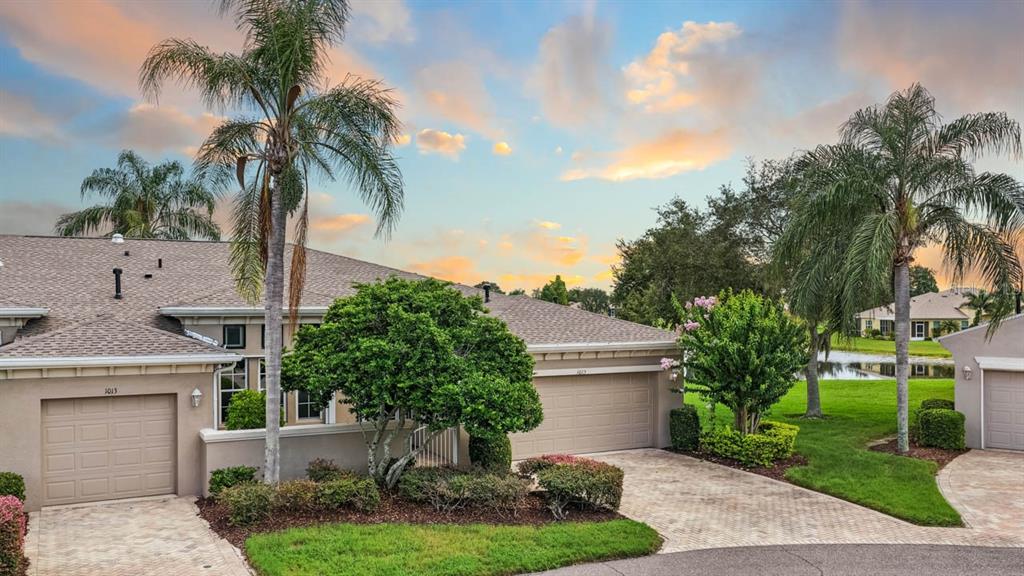 A residential exterior view featuring a paved driveway, two garage doors, and palm trees — 1015 CHELSEA GREENS COURT UNIT 40, SUN CITY CENTER, FL