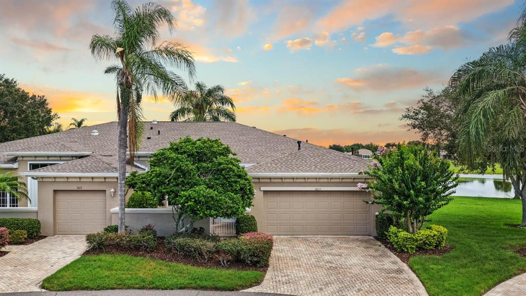 A single-story house with two garages, a paved driveway, and palm trees at sunset — 1015 CHELSEA GREENS COURT UNIT 40, SUN CITY CENTER, FL