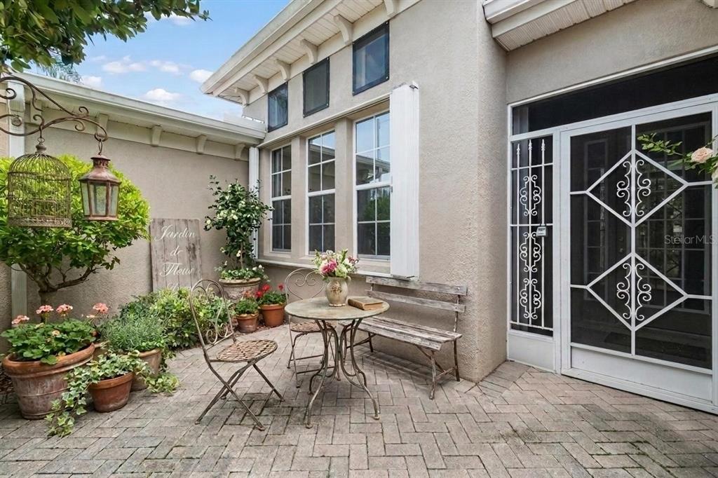 A patio with a bistro set, potted plants, and a decorative screen door — 1015 CHELSEA GREENS COURT UNIT 40, SUN CITY CENTER, FL