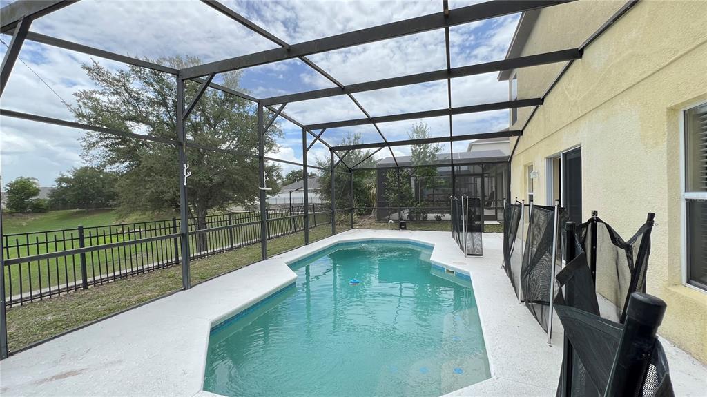 A swimming pool sits inside a screened-in patio enclosure next to a yellow house — 216 VERDI STREET, DAVENPORT, FL