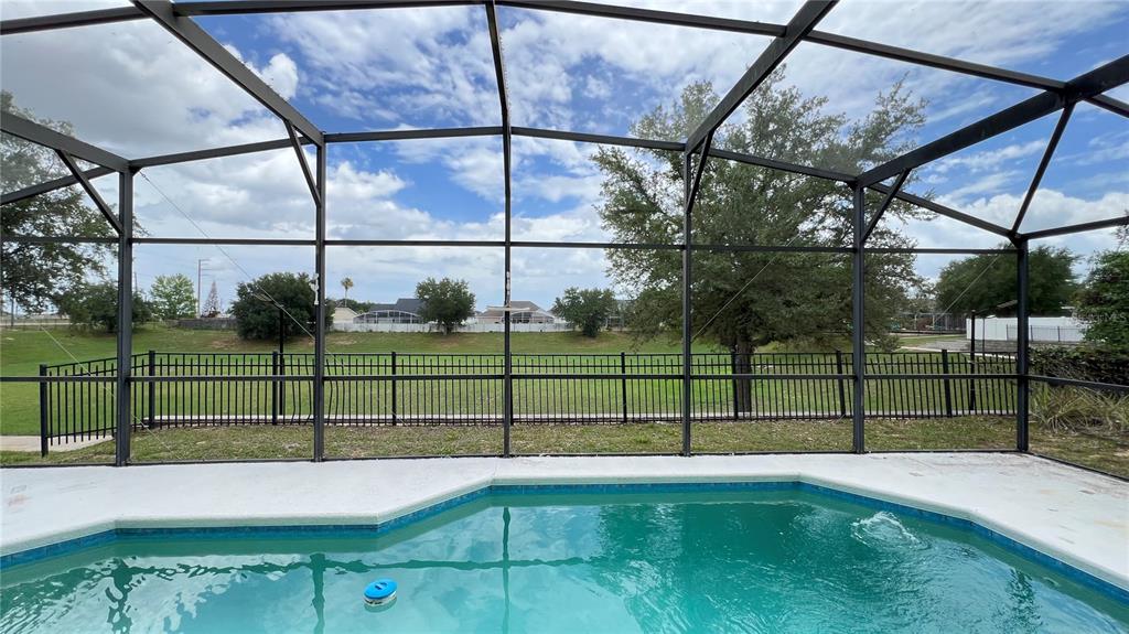 A swimming pool enclosed by a screened lanai overlooks a grassy yard and distant houses — 216 VERDI STREET, DAVENPORT, FL