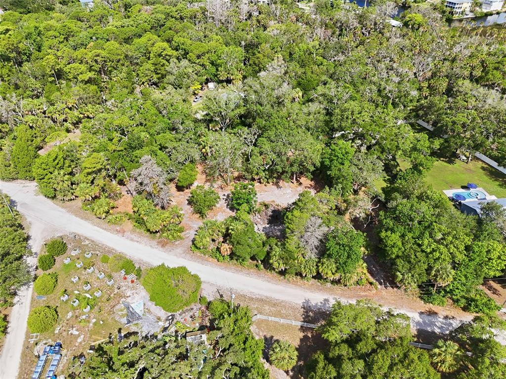 An aerial view shows a wooded, undeveloped lot bordered by a gravel road — JEBERT DRIVE, ARIPEKA, FL