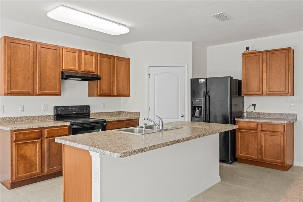 A kitchen features wood cabinets, a central island with a sink, and black appliances — 817 SHEEN CIRCLE, HAINES CITY, FL