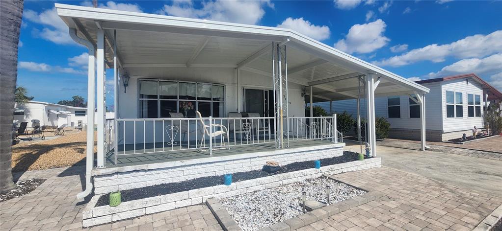 A mobile home features a covered front porch, white siding, and a paved patio area — 3229 TIKI DRIVE, HOLIDAY, FL
