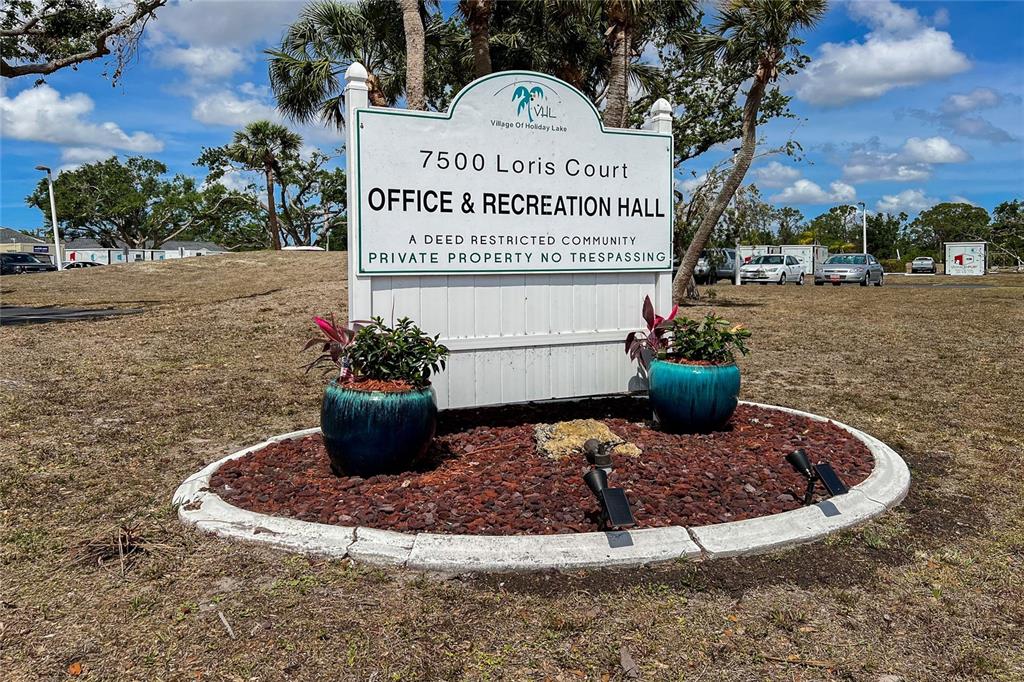 A sign for a community office and recreation hall stands in a landscaped garden bed — 7412 HESTON STREET, PORT CHARLOTTE, FL
