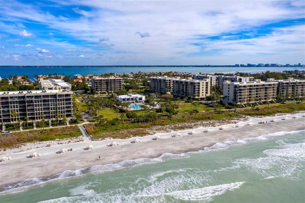 An aerial view shows beachfront apartment buildings with a swimming pool and surrounding palm trees — 1075 GULF OF MEXICO DRIVE UNIT 205, LONGBOAT KEY, FL