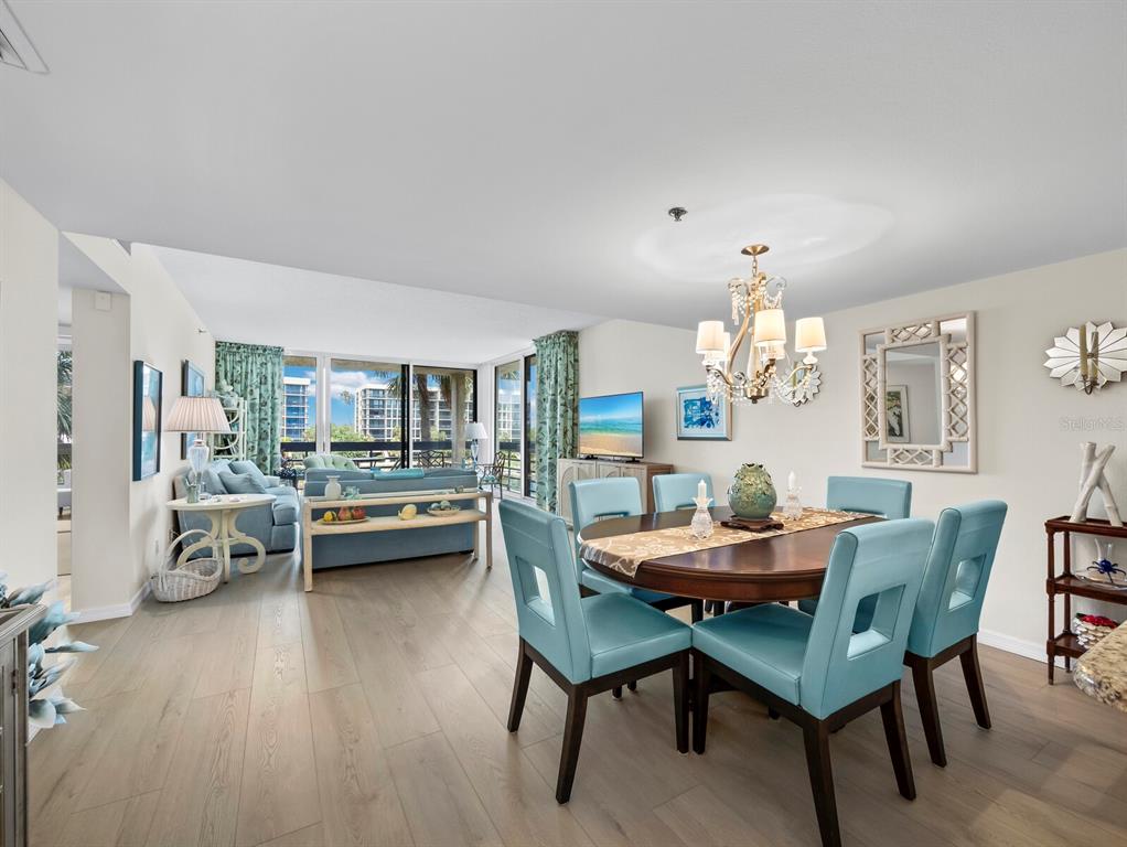 A dining area with a wooden table and blue chairs sits beside a living room — 1075 GULF OF MEXICO DRIVE UNIT 205, LONGBOAT KEY, FL