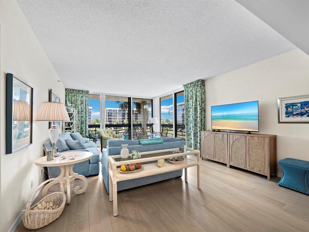 A living room features light wood flooring, a blue sofa, and a television on a console — 1075 GULF OF MEXICO DRIVE UNIT 205, LONGBOAT KEY, FL
