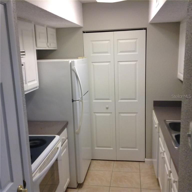 A galley kitchen features white cabinets, white appliances, dark countertops, and light-colored floor tiles — 3716 IDLEBROOK CIRCLE UNIT 110, CASSELBERRY, FL